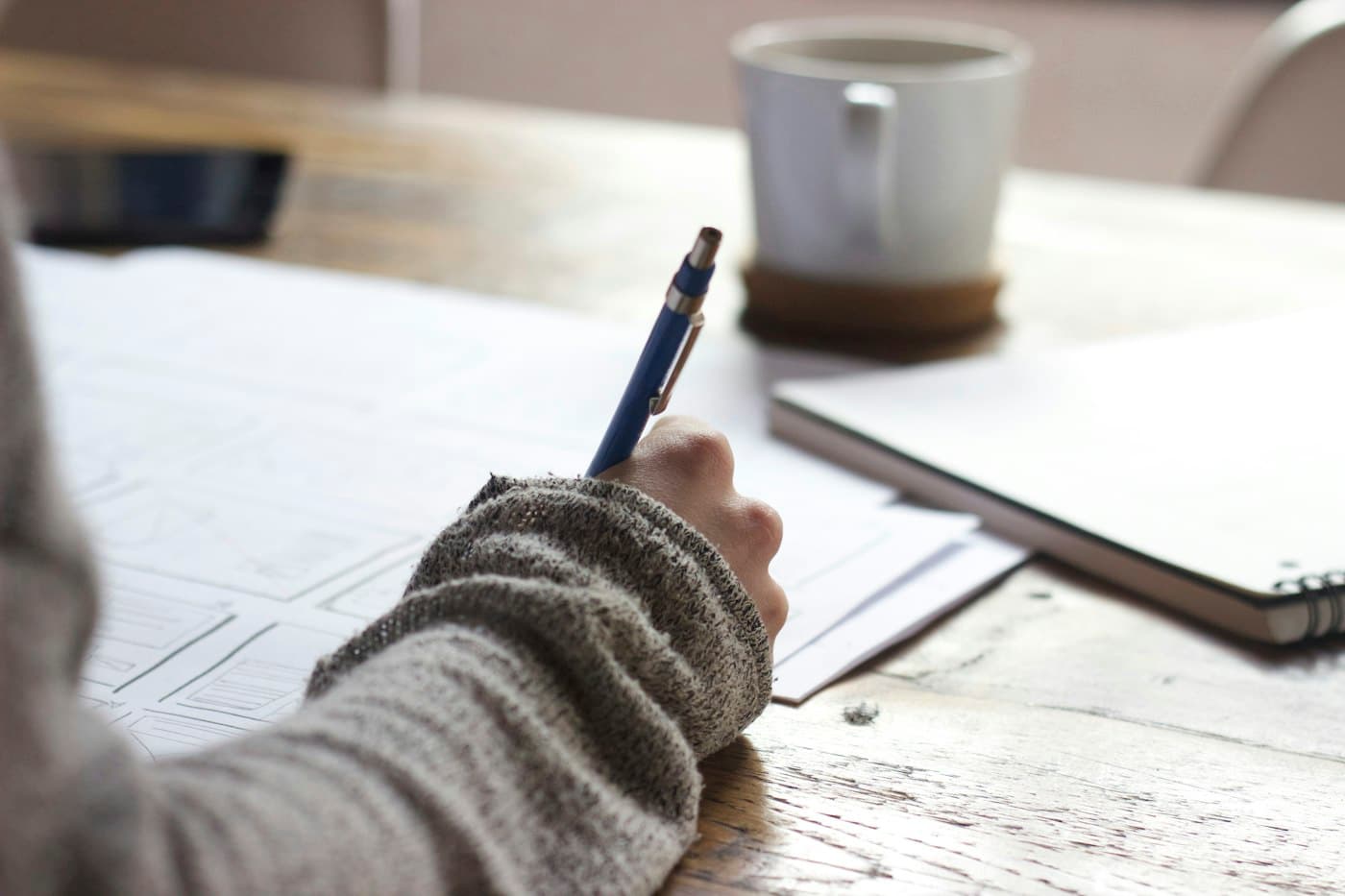 Estudante escrevendo num caderno, com livros abertos