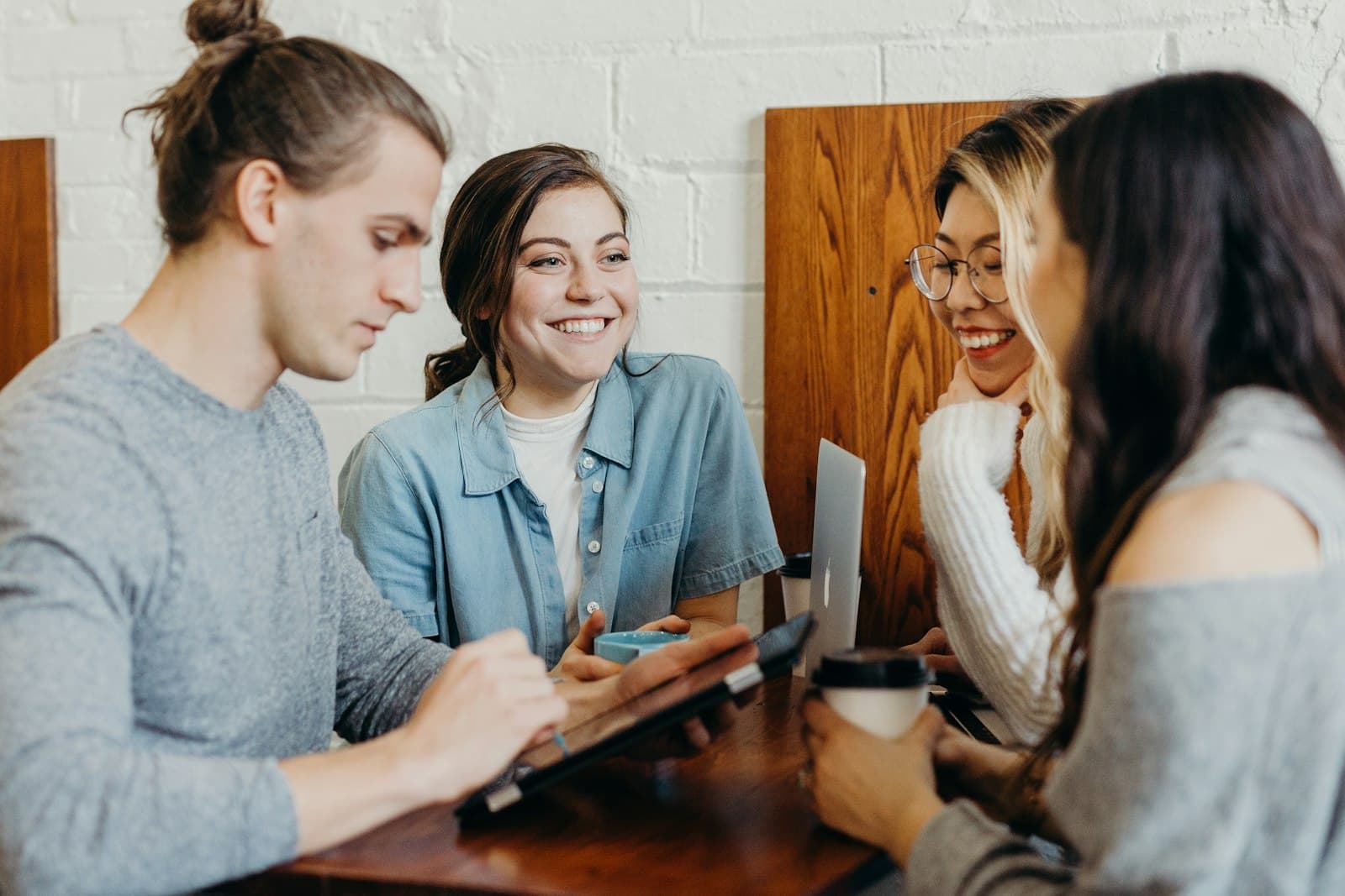 Estudantes sorrindo ao redor de uma mesa com notebook, tablet e café